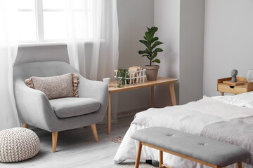 Interior of light bedroom with wooden table and armchair