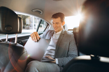 A modern businessman using a laptop computer while sitting in the back seat of a car.