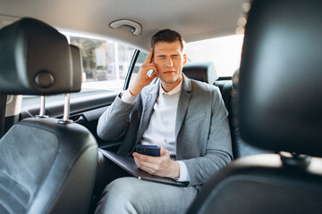 Fototapeta na wymiar Young businessman tired from work holding hand to his head while sitting in the back seat of the car.