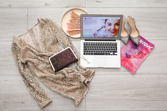 Laptop with fashion magazine and accessories of beauty blogger on wooden floor at home