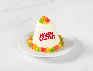 Festive dessert. Cottage cheese creamy Easter, decorated with colorful candied fruits, on a plate. Light background
