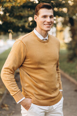 Obraz premium Modern handsome smiling man in yellow and white clothes posing in the park at sunset