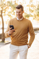 Modern handsome smiling man in yellow and white clothes talking on the phone in the park at sunset