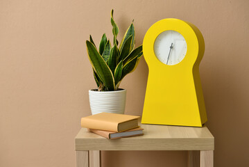 Table with modern clock, books and houseplant near color wall in room
