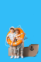 Funny little boys playing with cardboard ship and lifebuoy on blue background