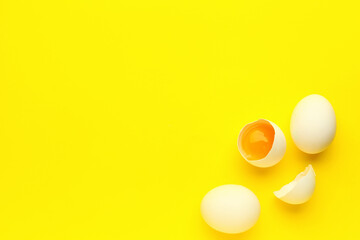 Cracked and whole chicken eggs on yellow background