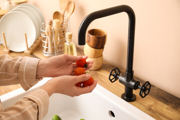 Woman washing cherry tomatoes over sink in kitchen, closeup