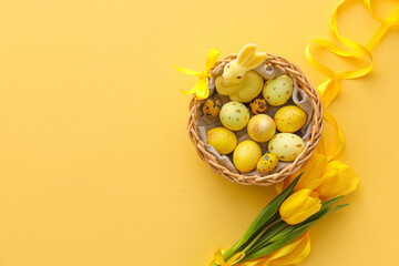 Basket with painted Easter eggs and bunny on yellow background