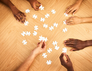 Soon it will all make sense. Cropped shot of a group of businesspeople completing a puzzle together on a table.