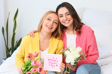 Young woman and her mother with flowers and greeting card for International Women's Day at home