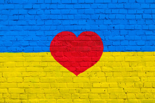 Brick wall is painted in the colors of the Ukrainian national flag - yellow and blue and red heart in the middle. Textured background. Symbol of love for Ukraine