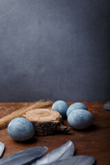 Blue painted easter eggs on brown wooden table with decorative silver feathers. Vertical shot, copy space