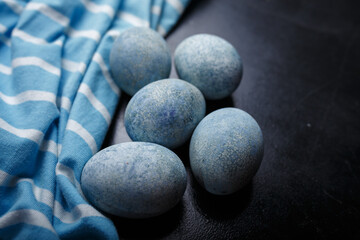 Easter eggs painted blue in white bowl on black wooden background with striped fabric. Close up shot, copy space