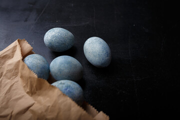 Easter eggs painted blue in craft paper bag on black wooden background. Top view, copy space