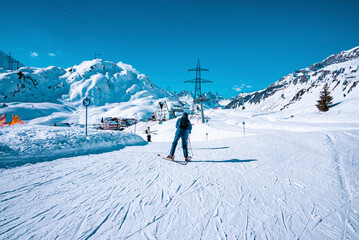Fototapeta na wymiar Skier skiing on snowy downhill. Tourist is leading toward houses on mountain against sky. He is enjoying winter sport in alps.