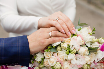 A newly weding couple place their hands on a wedding bouquet showing off their wedding rings.