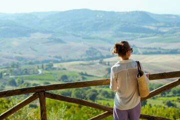 Seen from behind stylish woman with straw bag in Tuscany, Italy