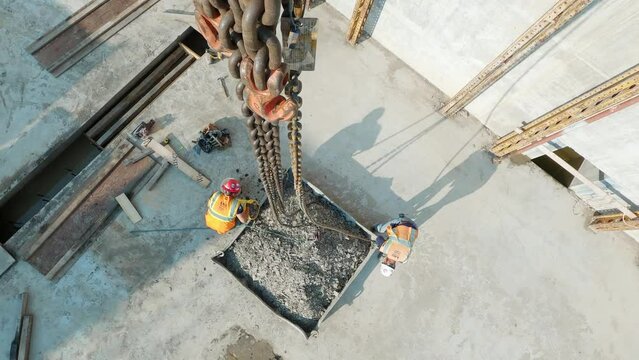 POV top down, construction workers connecting tower crane chains to container full of gravel at a construction site