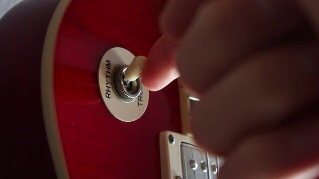 The pick-up switch of a red electric Les Paul guitar being switched from treble to rhythm. Static close-up shot