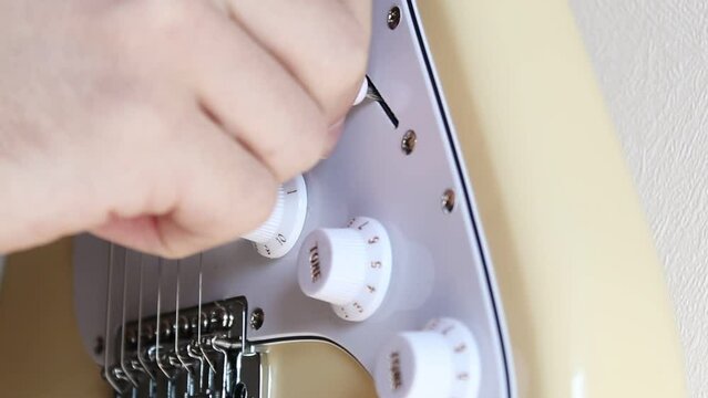 A hand moving the pick-up switch of a cream white electric stratocaster guitar. Static close-up shot