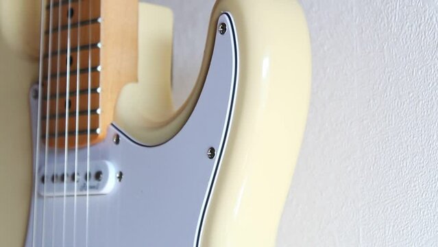 Close-up footage of a cream white stratocaster hanging off a white interior wall. Handheld pedestal shot