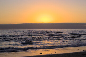 puesta de sol y ocaso en la orilla de playa con nubes en el horizonte y un pequeño bote