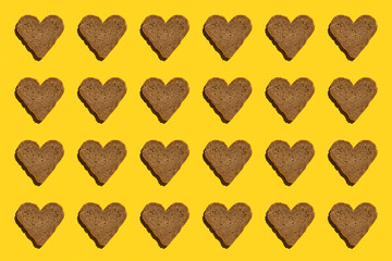 Pattern made with bread in heart form on yellow background, as backdrop or texture. Bright food wallpaper. Top view Flat lay