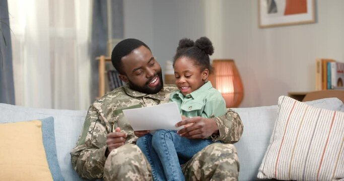 Positive military man reviewing photos with daughter at home