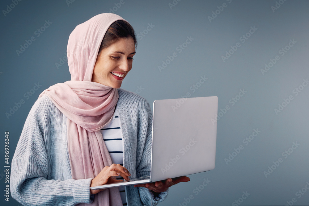 Poster She loves surfing the net. Studio shot of an attractive young woman using her laptop while standing against a grey background.