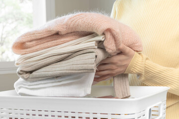 Housewife, asian young woman hand in many folding freshly shirts put the cloth in the basket after washing clean clothes and drying, making household working in room at home, maid chore laundry tidy.