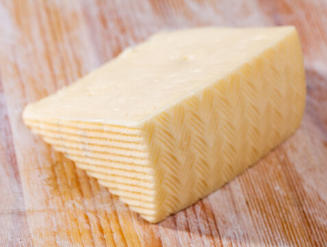 Slice of semi-soft cheese on a wooden table. High quality photo