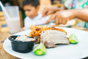 Close-up of a large piece of chicharron while a woman cuts meat to feed her son in the background