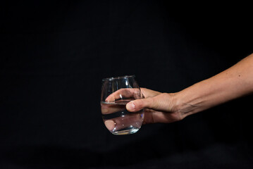 hand offering glass with pure water, black background