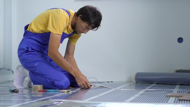 A professional master of underfloor heating installation connects the infrared heating film to the electric circuit