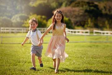 Naklejka na ściany i meble Siblings make the best friends. Portrait of a cute brother and sister running across a field while holding hands.