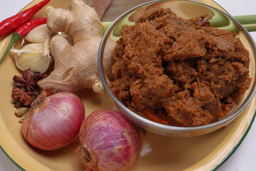 Traditional cooked beef meat rendang dry curry closeup in transparent glass bowl with ingredients...