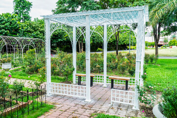 Metal gazebo with bench in public garden background. White steel pergola with fence in the park