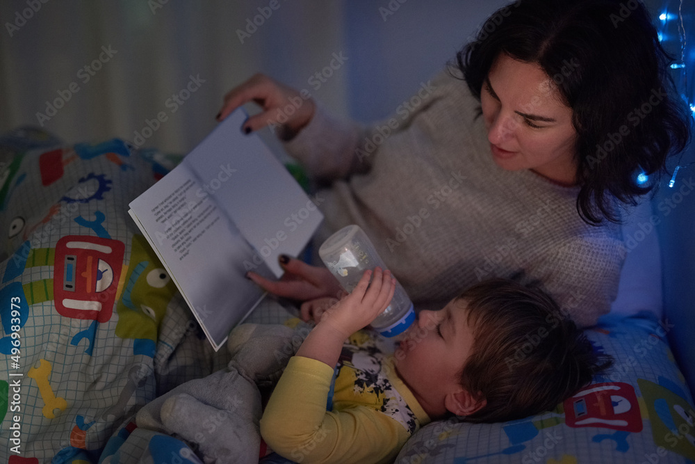 Sticker He always has his bottle and a book at bedtime. Cropped shot of a little boy lying in bed while his mom reads a bedtime story.