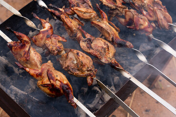 Cooking marinated quails on skewers, on the grill