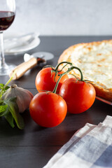 A view of a cluster of red ripe tomatoes on the vine, next to a pizza and other common Italian ingredients.