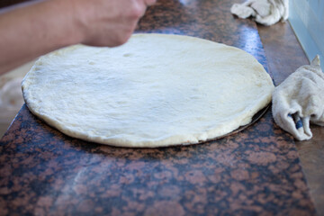 A view of a hand prepping a raw pizza dough on a restaurant kitchen counter.