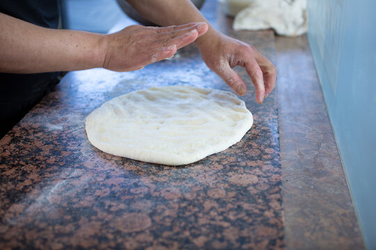 A view of a hand prepping a raw pizza dough on a restaurant kitchen counter.