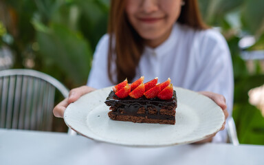 Closeup image of a young woman holding and eating a piece of strawberry chocolate cake