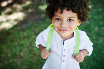 Im ready. Shot of a little boy wearing a backpack in nature.