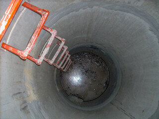 Looking into an open concrete manhole with step rungs leading down stagnant water