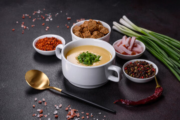 Cream soup with potatoes, leek and peas on a dark concrete table