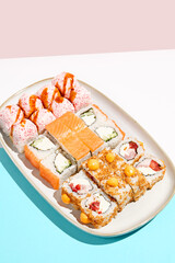 Set maki rolls on coloured background. Sushi roll assortment on ceramic plate. Maki sushi in minimal style. Japanese menu concept.