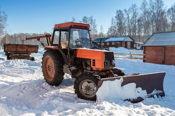 Orange wheeled snow plow tractor with blade in winter