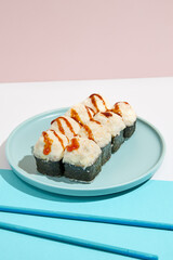 Baked Maki roll with shrimp and cheese on ceramic plate. Hot sushi roll with cheese topped on coloured background. Japanese menu concept. Hot sushi roll in modern style.