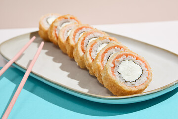 Baked Philadelphia Maki with salmon on ceramic plate. Hot tempura sushi with salmon and philadelphia cheese on coloured background. Japanese menu concept. Hot maki sushi in modern style.
